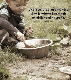 a little boy sitting in the grass playing with a metal bowl and spoon on top of it