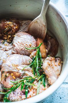 a white bowl filled with meat and vegetables next to a wooden spoon on top of a table