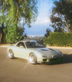 a white sports car parked in a parking lot with trees and bushes behind it on a sunny day