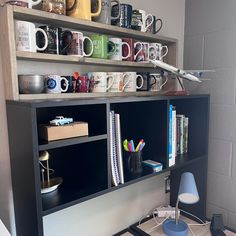 there is a desk with many coffee mugs on the top shelf and bookshelves above it