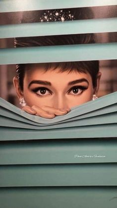 a woman's face peeking out from behind some blue shutters with her eyes open