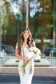 a woman is standing outside with flowers in her hand and she is wearing a white dress