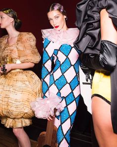 three women in dresses and hats standing next to each other at a fashion show with guitars on the floor