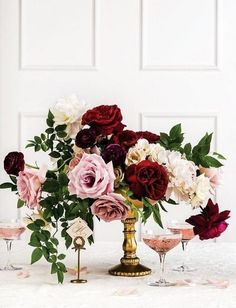 a vase filled with lots of flowers sitting on top of a table next to wine glasses