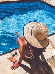 a woman sitting on the ground next to a pool with a bottle of booze