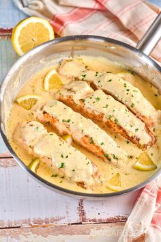 a pan filled with chicken covered in gravy and garnished with lemon slices