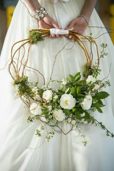 a woman in a white dress holding a flower crown with greenery and flowers on it