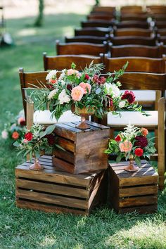 an arrangement of flowers and greenery are placed on wooden crates in front of the chairs