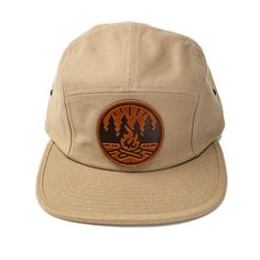 Get Fired Up for Adventure with this Campfire Cap! The patch on this hat features a classic campfire scene, capturing the timeless allure of the great outdoors. It's a simple yet evocative image: two logs ablaze with flames reaching upwards, cradled by a circle that hints at the unity and completeness of nature. The trees standing sentinel on either side anchor the scene in the wild, calling to mind the serenity of the woods and the simple pleasures of a fireside chat under the stars. Each cap i