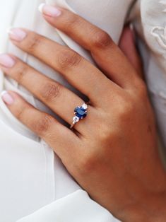 a woman's hand wearing a blue and white ring with an oval shaped diamond