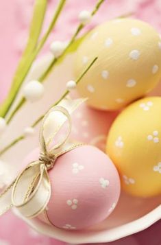 three painted eggs in a white bowl on a pink tablecloth with flowers and greenery