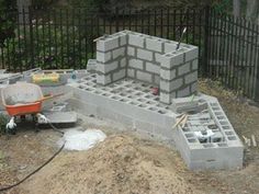 a cinder block structure being built in the yard with tools and supplies around it, including a wheelbarrow