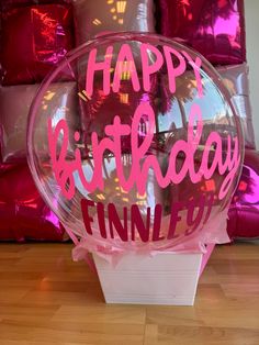 a happy birthday balloon with pink writing on it sitting in front of some foil balloons