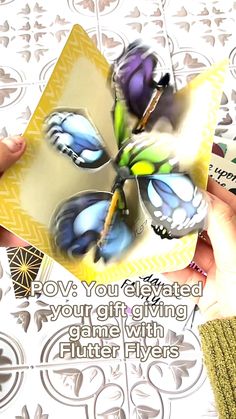 two hands holding a card with butterflies on it and the words, pov you are elevated in your gift giving game with flutter