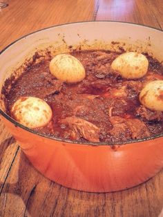 a pot filled with meat and potatoes on top of a wooden table