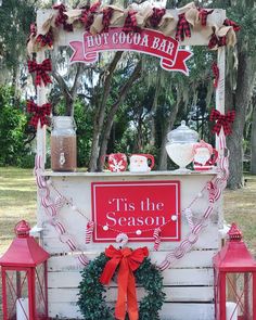 a hot cocoa bar decorated with red and white ribbon, wreaths, lights and lanterns