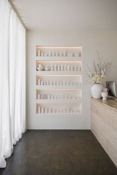 a white room with shelves and vases filled with flowers on the counter next to a window