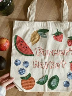 a person holding a tote bag on top of a wooden table next to fruit