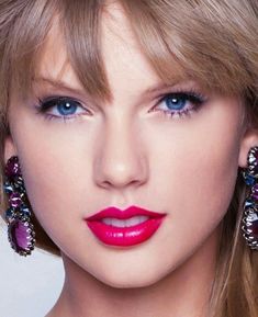 a close up of a woman with blue eyes and pink lipstick on her face, wearing large earrings