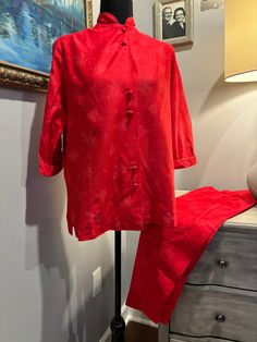 These LoungeCraft vintage PJ's/lounge wear are pristine! The red silky fabric has a subtle floral pattern. The top has a high collar and 3/4 length sleeves. There are covered buttons up the front with a snap at the collar. There is a slit on each side of the top. The ankle length, tailored pants have darts at the waistline. There is a metal zipper on the side that closes with a button at the waistband. There are slits at the ankle of the slacks.  Measurements taken with garment lying flat Top Shoulder to shoulder: 20" Pit to Pit: 20" Width at bottom: 23" Pants  Waist: 10 1/2 " (the button can be moved and a small dart at the back seam can be let out to give at least an additional inch to the waist ) Length: 35 1/2 " Womens Lingerie, Silky Fabric, Asian Inspired, Tailored Pants, Flats Top, Metal Zipper, Waist Length, Covered Buttons, High Collar