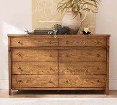 a wooden dresser with a potted plant sitting on top of it next to a white rug