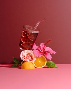 a pink background with flowers, oranges and a glass of wine on the table