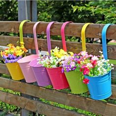 four buckets with flowers in them hanging on a fence