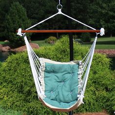 a blue and white hammock hanging from a wooden pole in front of some bushes