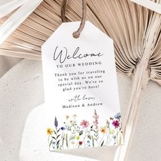 a welcome sign hanging from a palm tree with flowers on it and the words,'welcome to our wedding thank you for traveling