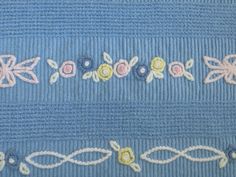 a blue blanket with flowers and braiding on the bottom, along with white thread