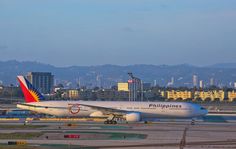 an airplane that is sitting on the tarmac in front of some buildings and mountains