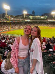 two women standing next to each other in front of a crowd at a baseball game