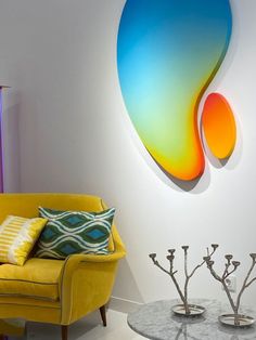 a yellow chair sitting in front of a wall with a colorful art piece on it