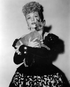 an old photo of a woman holding a small dog in her arms and looking at the camera