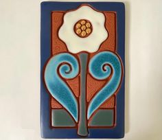 a blue and red tile with a flower on it's side, sitting on a white wall