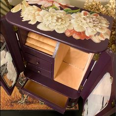 a purple cabinet with flowers painted on the side and drawers open to show items inside