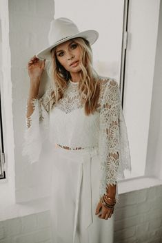 a woman wearing a white hat standing in front of a window with her hand on her hip