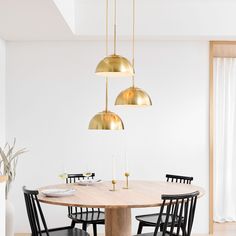 a dining room table with four chairs and three pendant lights hanging from it's ceiling