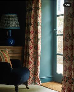 a chair sitting in front of a window next to a lamp and curtained wall