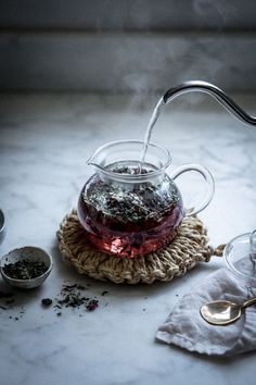 a glass tea pot filled with water on top of a table next to two spoons