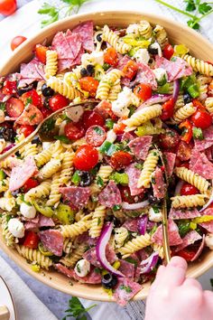 a large bowl filled with pasta salad on top of a white table next to other food items