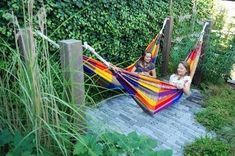 two women sitting in hammocks on a brick walkway next to green plants and bushes