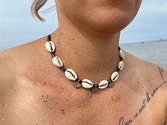 BOHO CHOKER NECKLACE with cowrie shells and brass pendants/beads and wooden elements. Surfer - boho jewelry. The length is adjustable with a slide closure. So you can wear the necklace as a choker close to your neck, or as a long necklace. You can also find a matching bracelet in the shop. Length adjustable from approx. 35 - 70cm Material: waxed macrame ribbon, cowrie shells, brass pendant, brass beads. You are very welcome to leave individual inquiries here or by e-mail. Macrame Ribbon, Wooden Bead Jewelry, Cowrie Shell Jewelry, Boho Choker Necklace, Cowrie Shell Necklace, Brass Pendants, Shell Choker, Choker Chain, Cowrie Shells