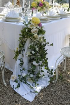 the table is set with white and yellow flowers, greenery, and silverware