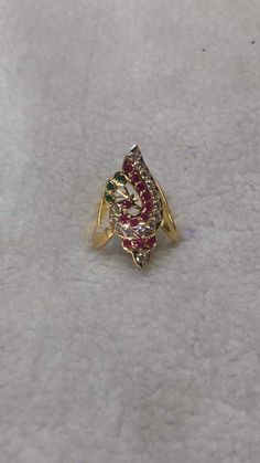 a gold ring with red, green and white stones on it's side sitting on a surface