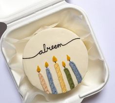 a birthday cake with candles on it sitting in a white container that says alween