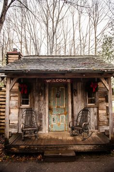 an old log cabin with rocking chairs on the front porch and welcome sign above the door