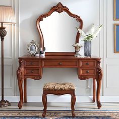 a dressing table with a mirror, stool and lamp in a white walled room next to a painting on the wall