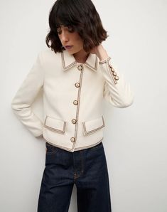 a woman in a white jacket and jeans is leaning against a wall with her hand on her head