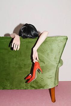 a woman is sitting on a green couch with her head resting on the back of a chair